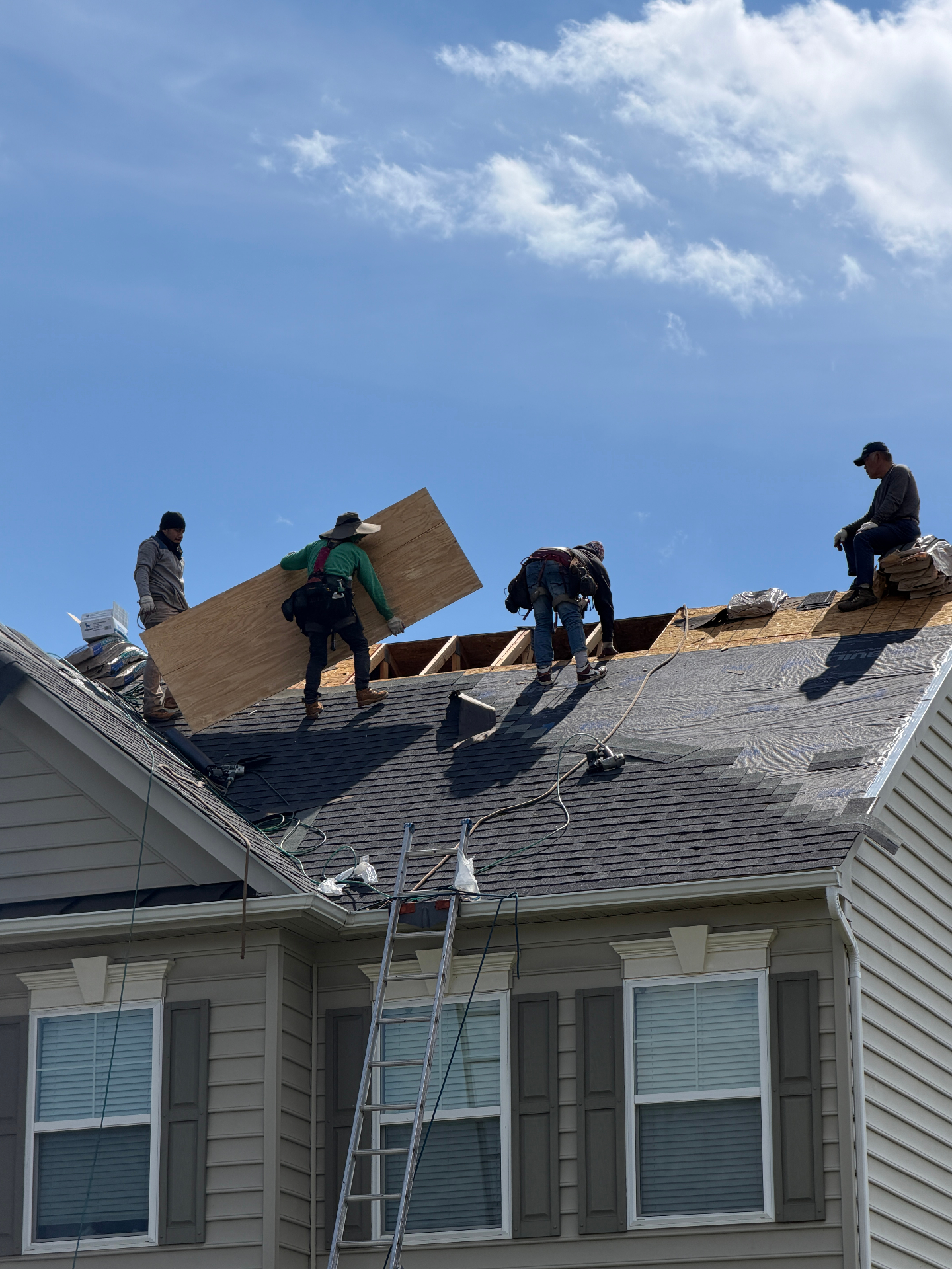 The Perpetual Improvements crew on a Northern Virginia rooftop, hauling new decking onto a tear-off under a bright blue sky.